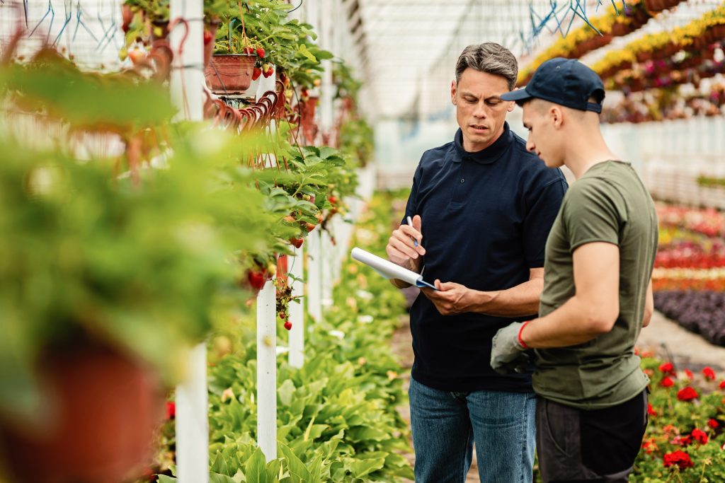 Quality control inspector and worker talking while going through list of plants in a greenhouse.